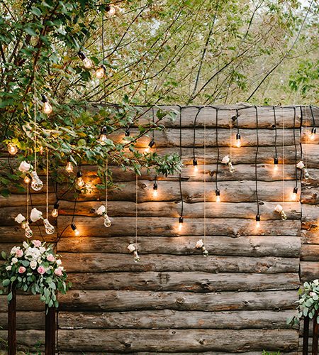 Wooden wall decorated garland with luminous bulbs and electric lamps decorated flowers. Original wedding floral decoration.  Wedding. Reception. Lounge zone.